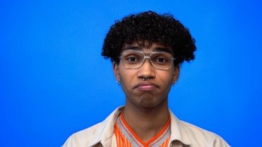 Gözlüklü Afro-Amerikan adam mavi kameraya bakıyor. 