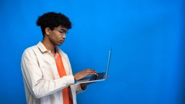 Genç Afro-Amerikan gözlüklü, mavi ekranda izole edilmiş dizüstü bilgisayar kullanan. 