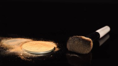 Siyah yüzeyde bej yüz pudrası yakınında kozmetik fırçası 