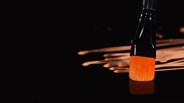 Close up view of cosmetic brush near blurred makeup foundation on black background 