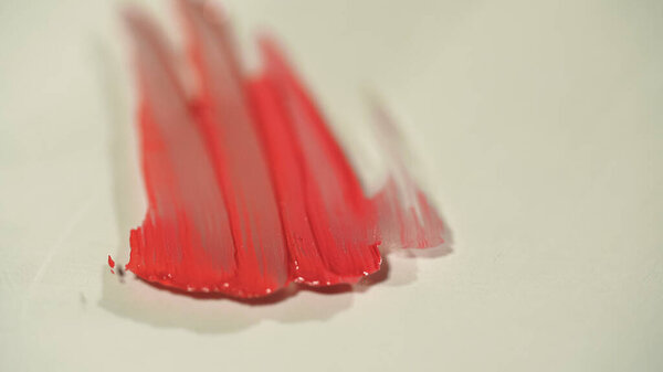Close up view of red lip gloss strokes on grey surface 