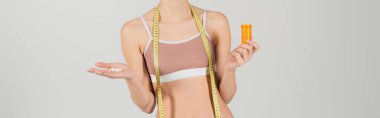 Gri pankartta izole edilmiş vitaminlerle ölçüm yapan genç bir kadının kısmi görüntüsü