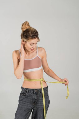 Gülümseyen ve formda spor elbiseli bir kadın. Gri üzerinde izole edilmiş bel ölçüsünde.
