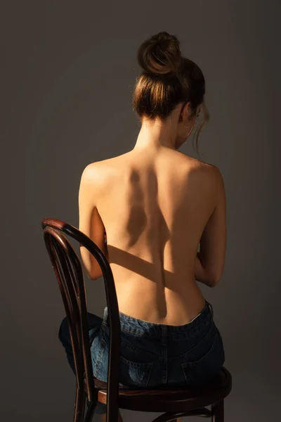 back view of half nude woman in jeans sitting on wooden chair isolated on grey