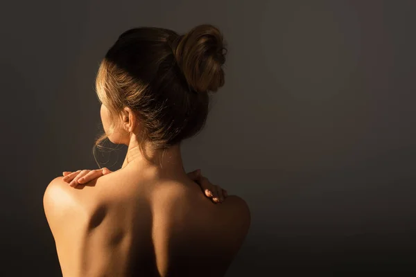 back view of nude woman with perfect body touching shoulders isolated on grey