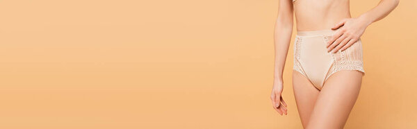 cropped view of fit woman touching lace panties isolated on beige, banner