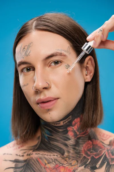 Homem Jovem Tatuado Aplicando Soro Hidratante Isolado Azul — Fotografia de Stock