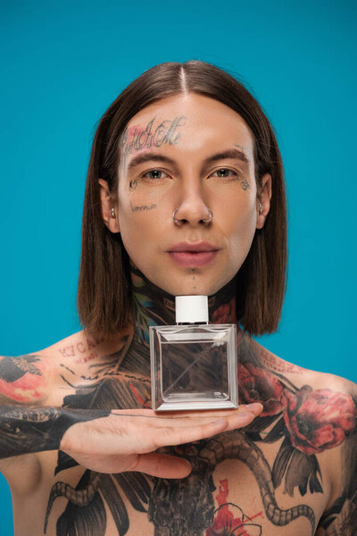 shirtless and tattooed man holding bottle with perfume isolated on blue