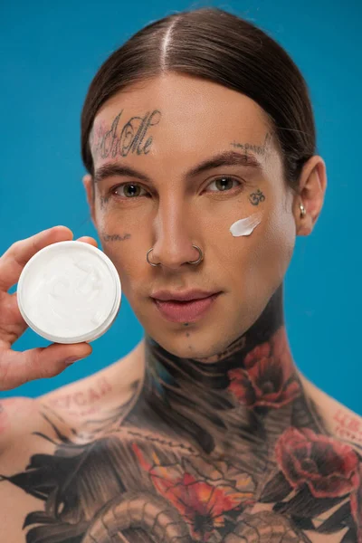 Jovem Tatuado Com Creme Bochecha Segurando Recipiente Isolado Azul — Fotografia de Stock