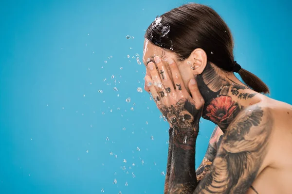 Stänk Vatten Nära Man Med Tatueringar Tvätta Ansiktet Isolerat Blått — Stockfoto