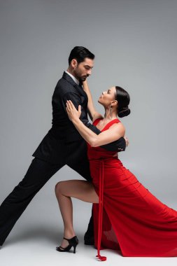 Gri arka planda partneriyle dans eden esmer kadın.