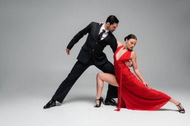 Takım elbiseli adam, gri arka planda tango yaparken partnerine sarılıyor.