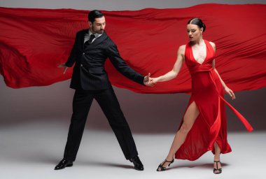 Professional ballroom dancers holding hands on grey background with red fabric  clipart