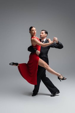 Kırmızı elbiseli şık bir kadın, gri arka planda bir adamla tango yapıyor.