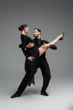 Profesyonel dansçılar, gri arka planda tango yaparken birbirlerine bakarlar.
