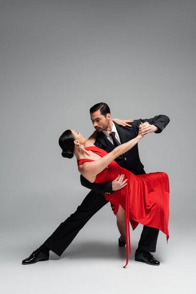 Elegant man in suit dancing tango with partner on grey background