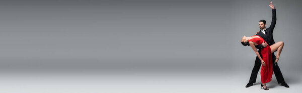 Профессиональная бальная танцовщица позирует во время танго с партнером на сером фоне, баннер 