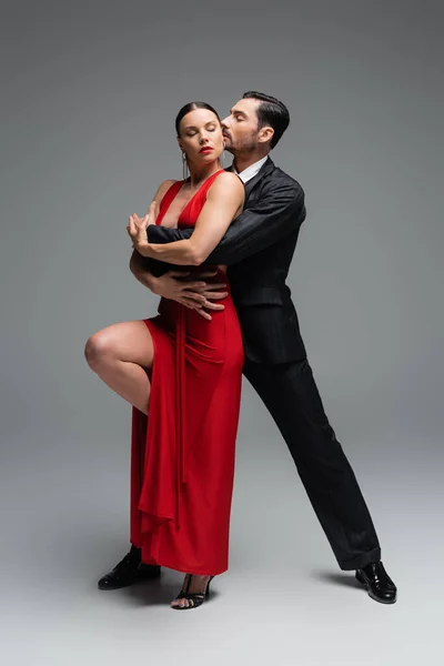 Professional dancers performing tango with closed eyes on grey background