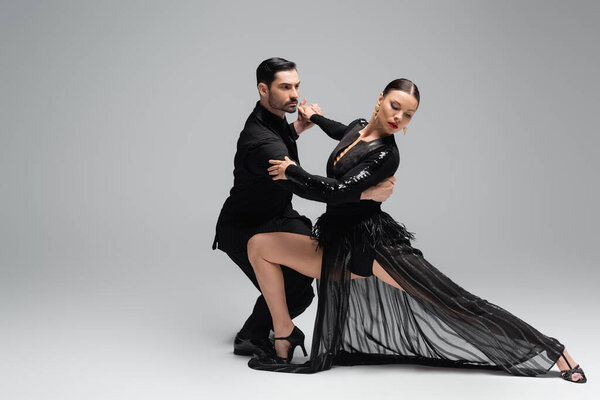 Man in suit dancing with partner in black dress on grey background