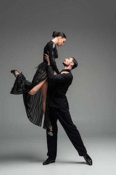 Side view of professional ballroom dancer lifting partner on grey background