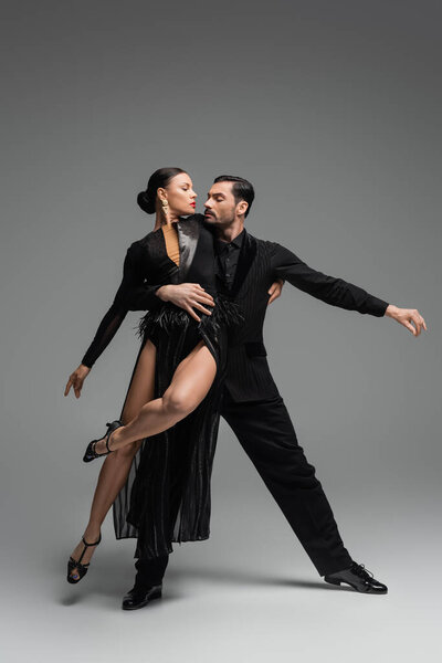 Professional ballroom dancers in black costumes performing tango on grey background