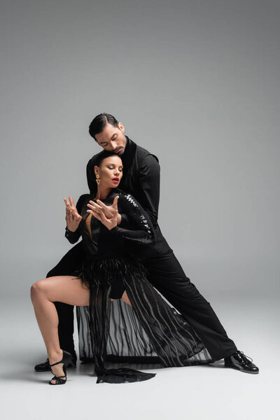 Elegant dancer performing tango with partner in black dress on grey background