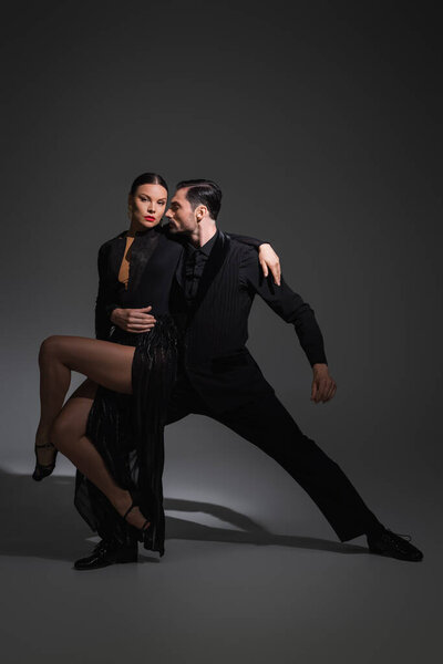 Dancer in suit hugging partner with red lips while performing tango on grey background with shadow 