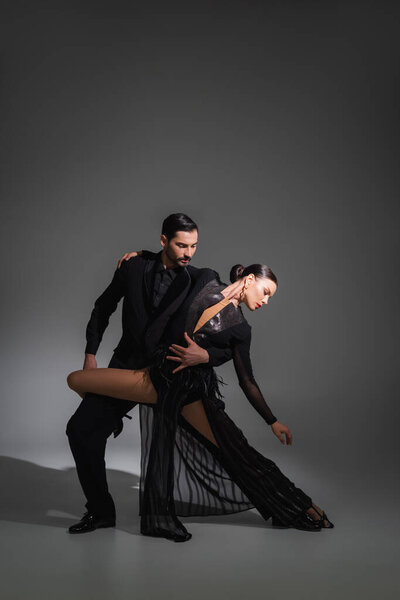 Elegant dancer hugging brunette partner in black dress on grey background with lighting 