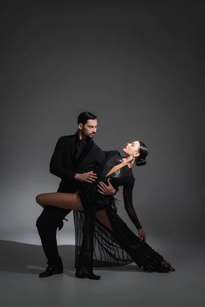 Elegant couple dancing tango on grey background with shadow