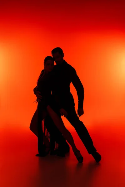 Silhouette of ballroom dancers performing tango on red background