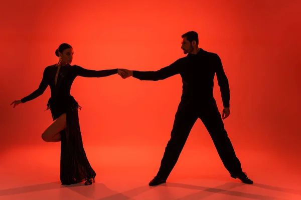 Silhouette of ballroom dancers holding hands on red background with shadow