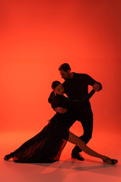 Silhouette of man in suit dancing tango with woman in dress on red background 