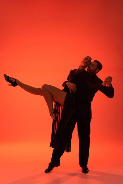 Elegant woman holding hands while dancing tango on red background with shadow 