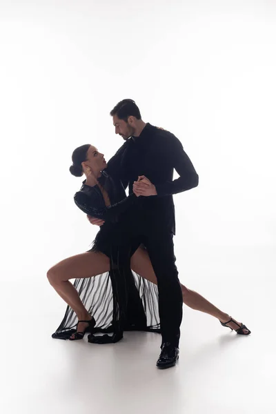 Side view of professional dancers holding hands while performing tango on white background