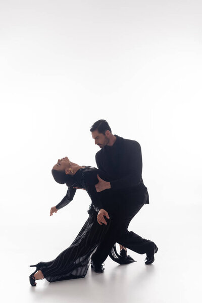 Couple in suit and dress performing tango on white background 