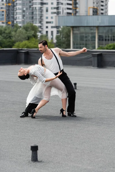 Professional dancer moving with elegant partner on rooftop of building outdoors