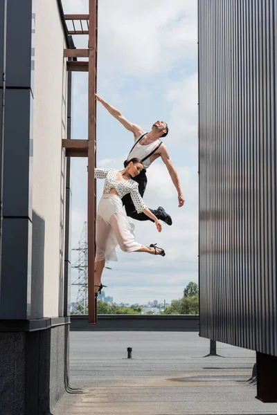 Cheerful professional dancers posing on ladder on roof of building outdoors