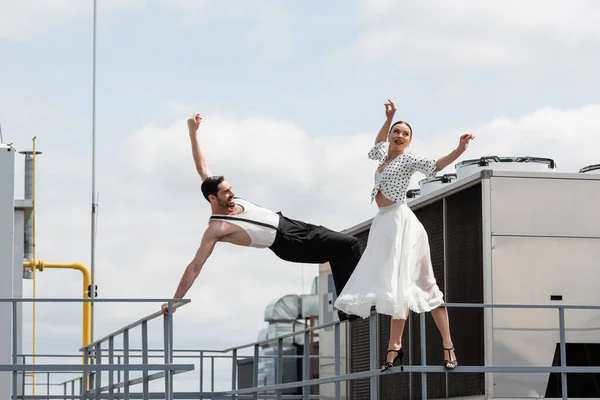 Cheerful professional dancers moving near railing on roof of building outdoors