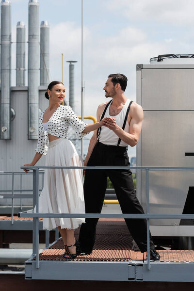 Стильные профессиональные танцоры, держащиеся за руки возле перила на крыше здания на открытом воздухе 