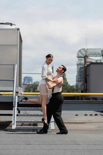 Professional dancer lifting partner while dancing on roof of building at daytime