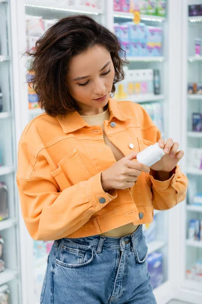 Client brunette regardant bouteille avec des médicaments en pharmacie — Photo de stock