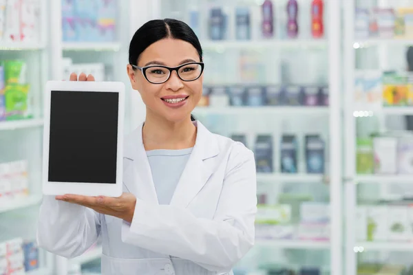 Positif asiatique pharmacien dans lunettes tenant numérique comprimé avec écran vierge en pharmacie — Photo de stock