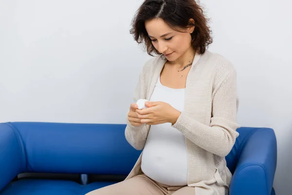 Femme enceinte avec tatouage regardant bouteille avec des vitamines tout en étant assis dans la pharmacie — Photo de stock