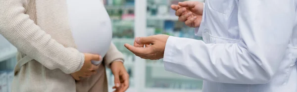 Vue recadrée du pharmacien gesticulant près de la femme enceinte en pharmacie, bannière — Photo de stock