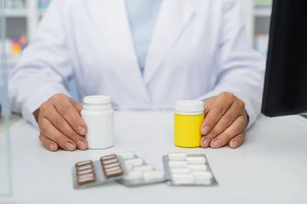 Vista recortada del farmacéutico sosteniendo frascos con medicamentos cerca de blisters - foto de stock