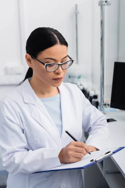 Asiatischer Apotheker in Brille mit Klemmbrett beim Schreiben in der Drogerie — Stockfoto