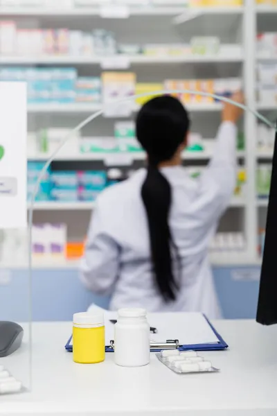 Bottles and blister pack with medication near blurred pharmacist on background — Stock Photo