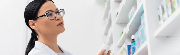 Asian pharmacist in glasses looking at medication in drugstore, banner — Stock Photo