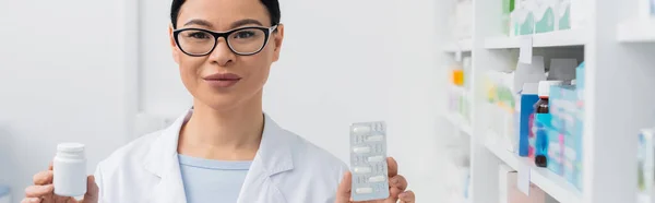 Farmacéutica asiática complacido celebración botella y blíster paquete con medicamentos, bandera — Stock Photo