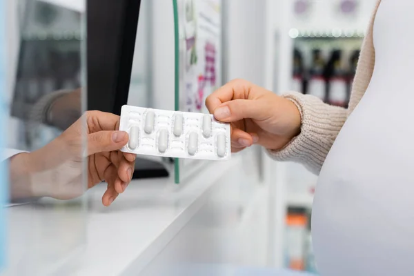 Vista recortada del farmacéutico que administra blíster con medicamento al cliente embarazada - foto de stock